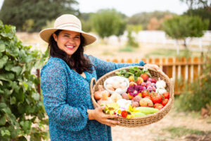 woman wearing sun hat holding basket of vegetables and fruit